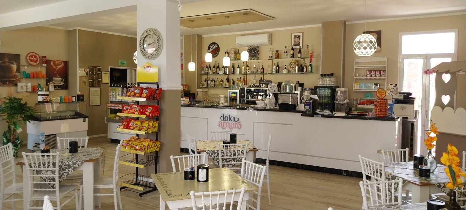 La sala di Dolce Amaro: il lungo bancone bianco, l'orologio sulla colonna e i tavolini apparecchiati con le tovaglie damascate